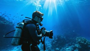 Scuba diver equipped with professional underwater photography equipment, preparing to photograph a vibrant coral reef with sunlight beams illuminating the ocean depth.