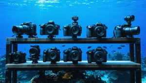 A collection of underwater photography equipment including cameras, housing systems, and lighting setups against a deep ocean backdrop, showcasing essential gear for capturing stunning underwater images.
