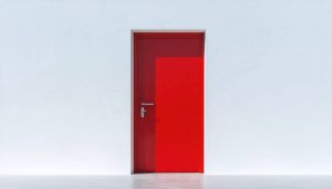 Solitary red door centered on a vast white wall, exemplifying minimalist photography through contrasting color and expansive negative space.