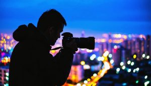 Professional photographer taking a cityscape photo at twilight with a fast zoom lens, emphasizing low-light photography.