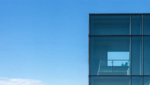 Minimalist architectural photograph showcasing geometric patterns of a glass building with a solitary window against a clear blue sky, emphasizing clean lines and negative space.