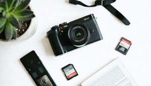 A compact and stylish point-and-shoot camera sits on a desk with photography essentials, including memory cards and a user manual, symbolizing user-friendliness and accessibility for beginners.