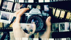 A creative double exposure image showcasing a vintage camera being used, overlaid with film rolls and negatives, capturing the essence of film photography's uniqueness.