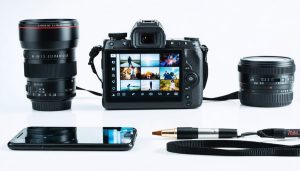 Smartphone and professional camera aimed at a colorful Instagram feed displayed on a digital screen, surrounded by editing tools like sliders and color wheels.