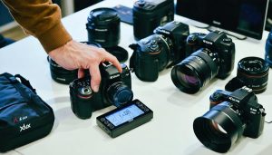 Photographer using xlux moisture meter to check moisture levels of camera gear in an organized workstation, highlighting the device's precision in protecting valuable equipment from humidity damage.