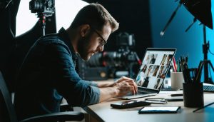 "Photographer engaged in photo editing using AI software on a laptop, surrounded by professional studio equipment."