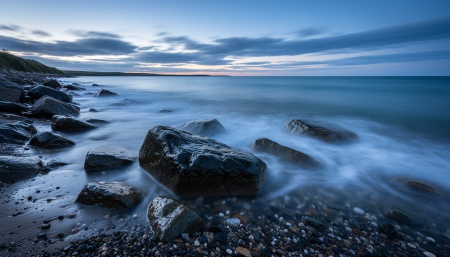 Long exposure photograph showing smooth flowing water around rocks with coastal cliffs